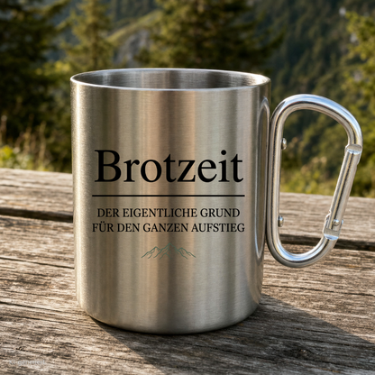 Karabinertasse von Kraxelgaudi mit Brotzeit Motiv steht auf Holz vor Bergkulisse