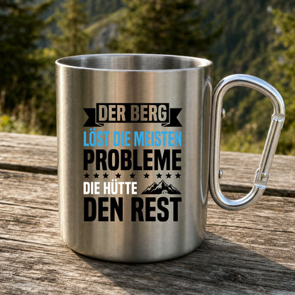 Karabinertasse von Kraxelgaudi mit Spruch Der Berg löst die meisten Probleme steht auf Holz vor Bergkulisse