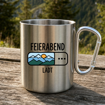 Karabinertasse von Kraxelgaudi mit Motiv Feierabend lädt steht auf Holz vor Bergkulisse