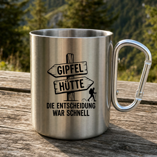 Karabinertasse von Kraxelgaudi mit Wegweiser Gipfel oder Hütte steht auf Holz vor Bergkulisse
