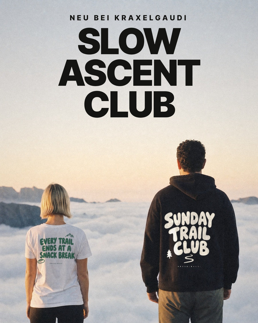 Paar von hinten über dem Wolkenmeer: sie im weißen Shirt mit grünem Rückendruck, er im schwarzen Hoodie mit Rückendruck, darüber der Schriftzug Slow Ascent Club. Bild mit KI erstellt.