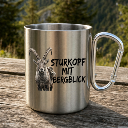 Karabinertasse von Kraxelgaudi mit Steinbock und Spruch Sturkopf mit Bergblick steht auf Holz vor Bergkulisse